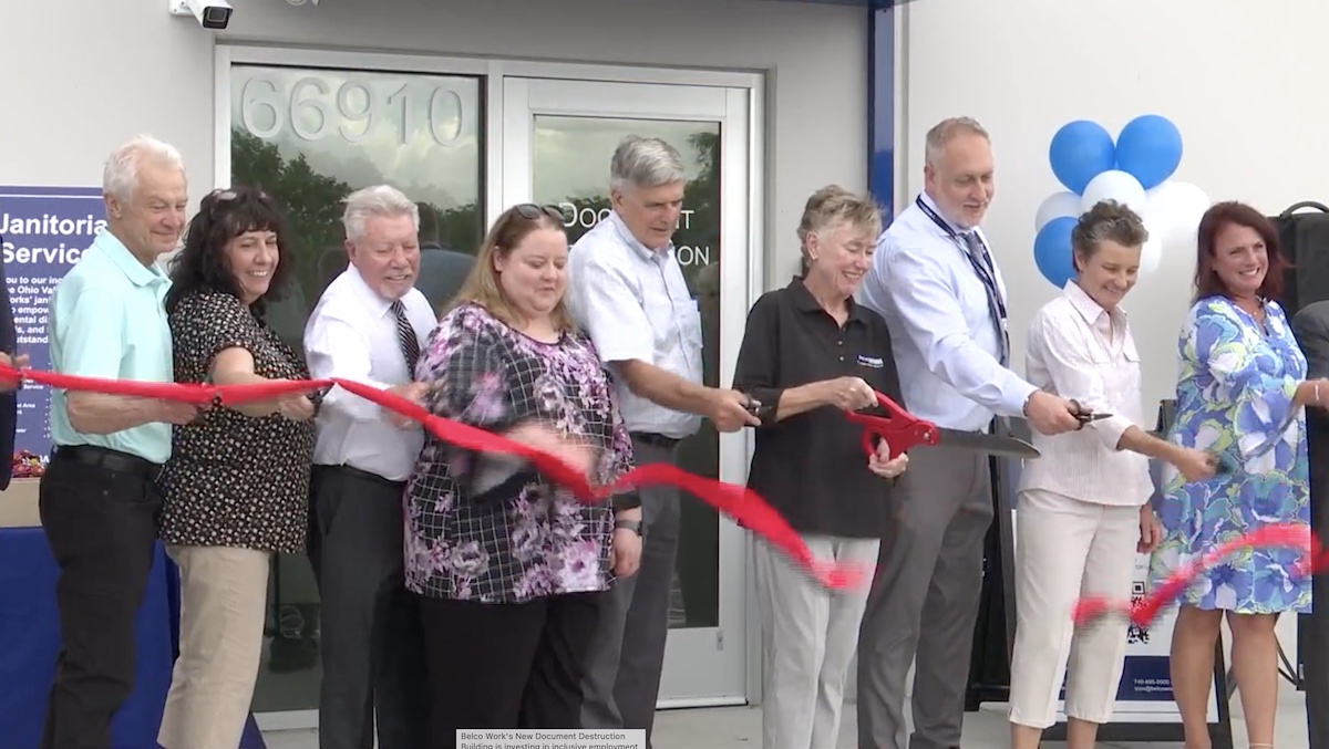 Nine people cutting a red ribbon in front of the Belco Document Destruction building.