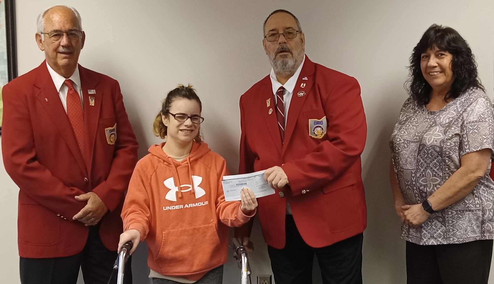 Two people in red jackets handing a check to a person using a walker